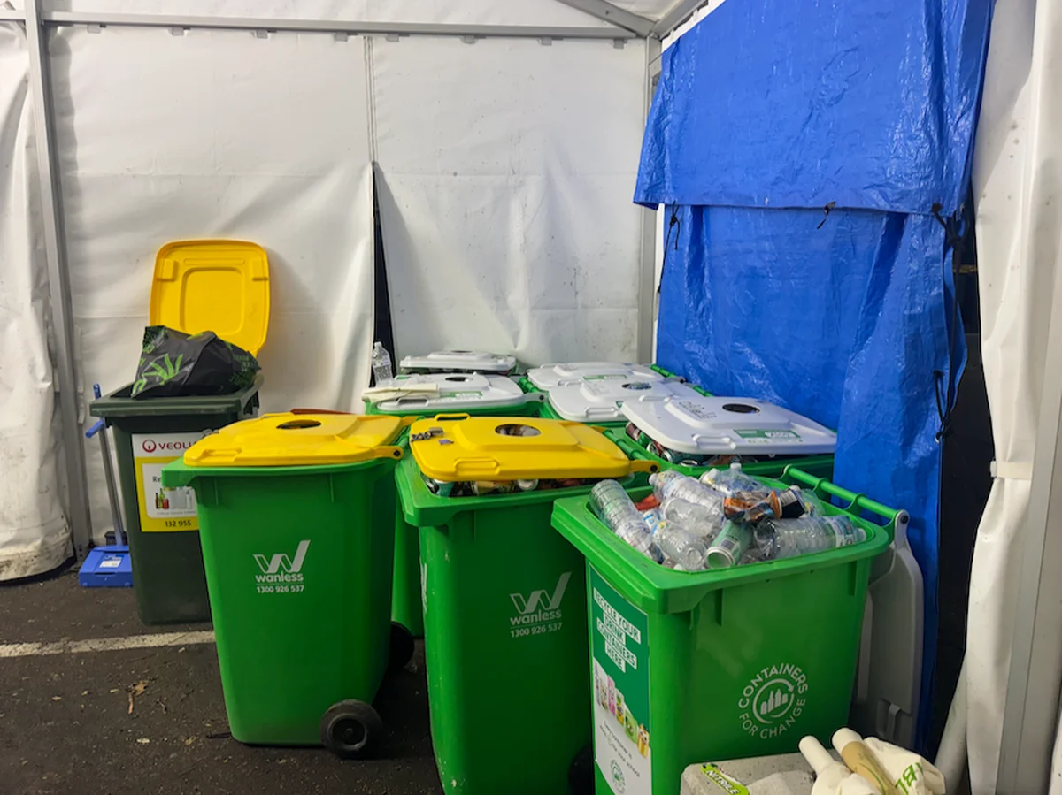 Separated green recycling and organics bins arranged inside a back-of-house waste tent at an event