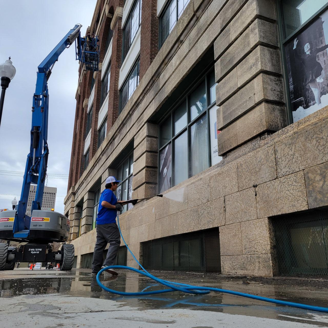 New Era team member pressure-washing the stone facade of a commercial building with a boom lift positioned alongside