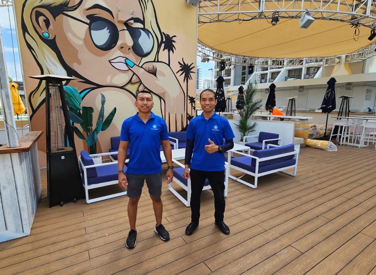Two New Era team members in branded blue polos standing on the timber deck of a rooftop venue they service