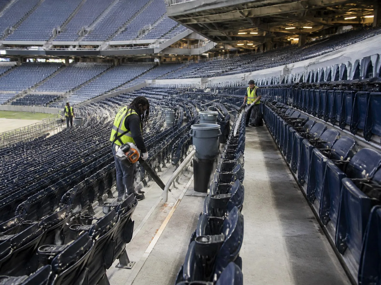 Crew in high-visibility vests clearing a stadium seating bowl and concourse between events, representative of major venue turnaround work