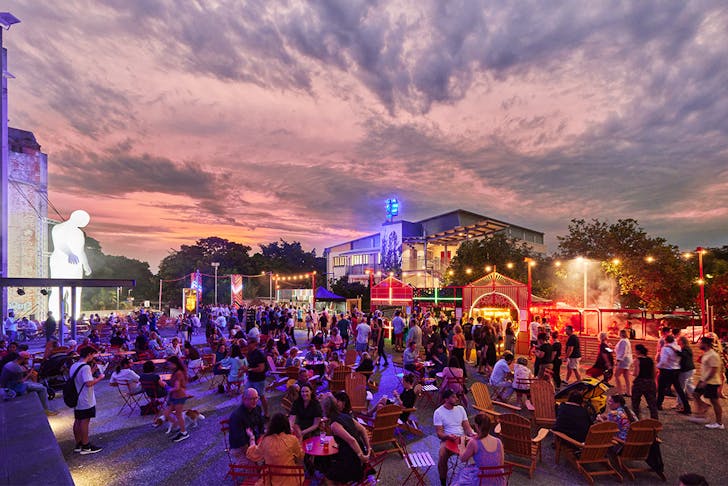Night Feast event precinct at dusk with guests seated across the open forecourt