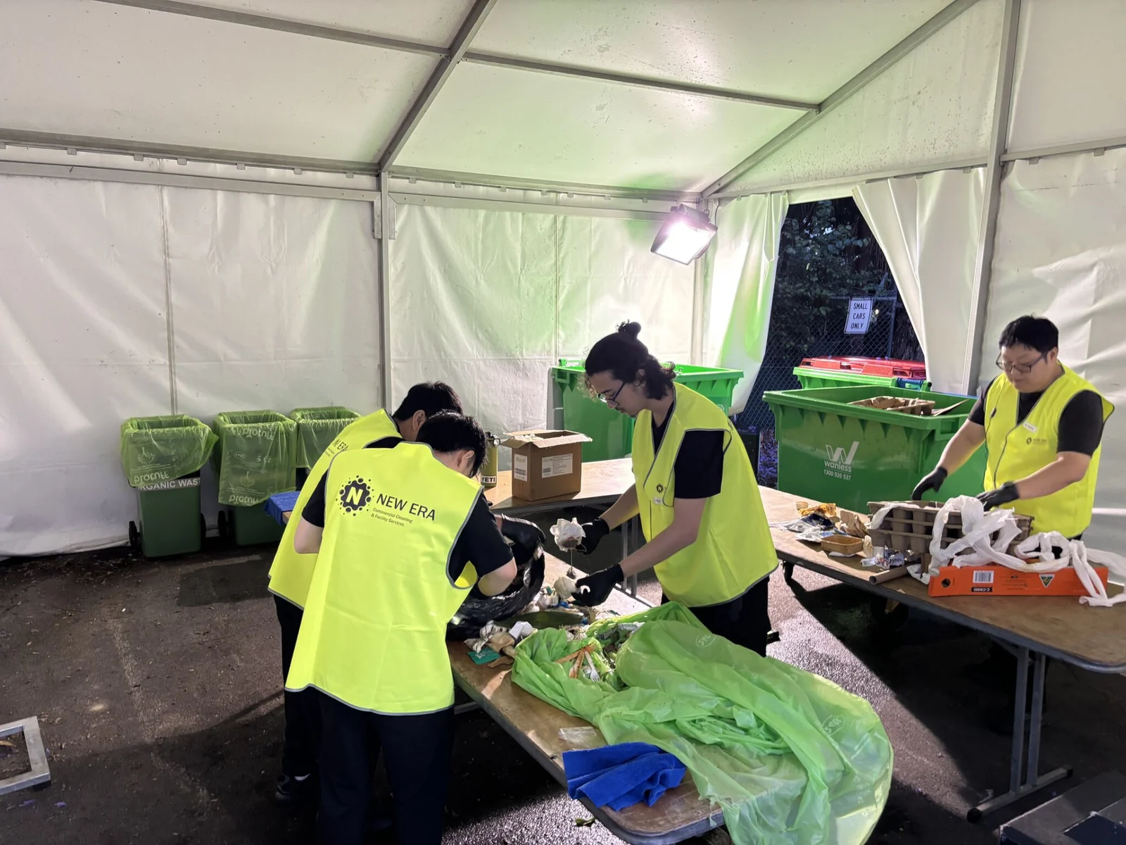New Era team members in high-visibility vests hand-sorting event waste at tables inside a back-of-house marquee