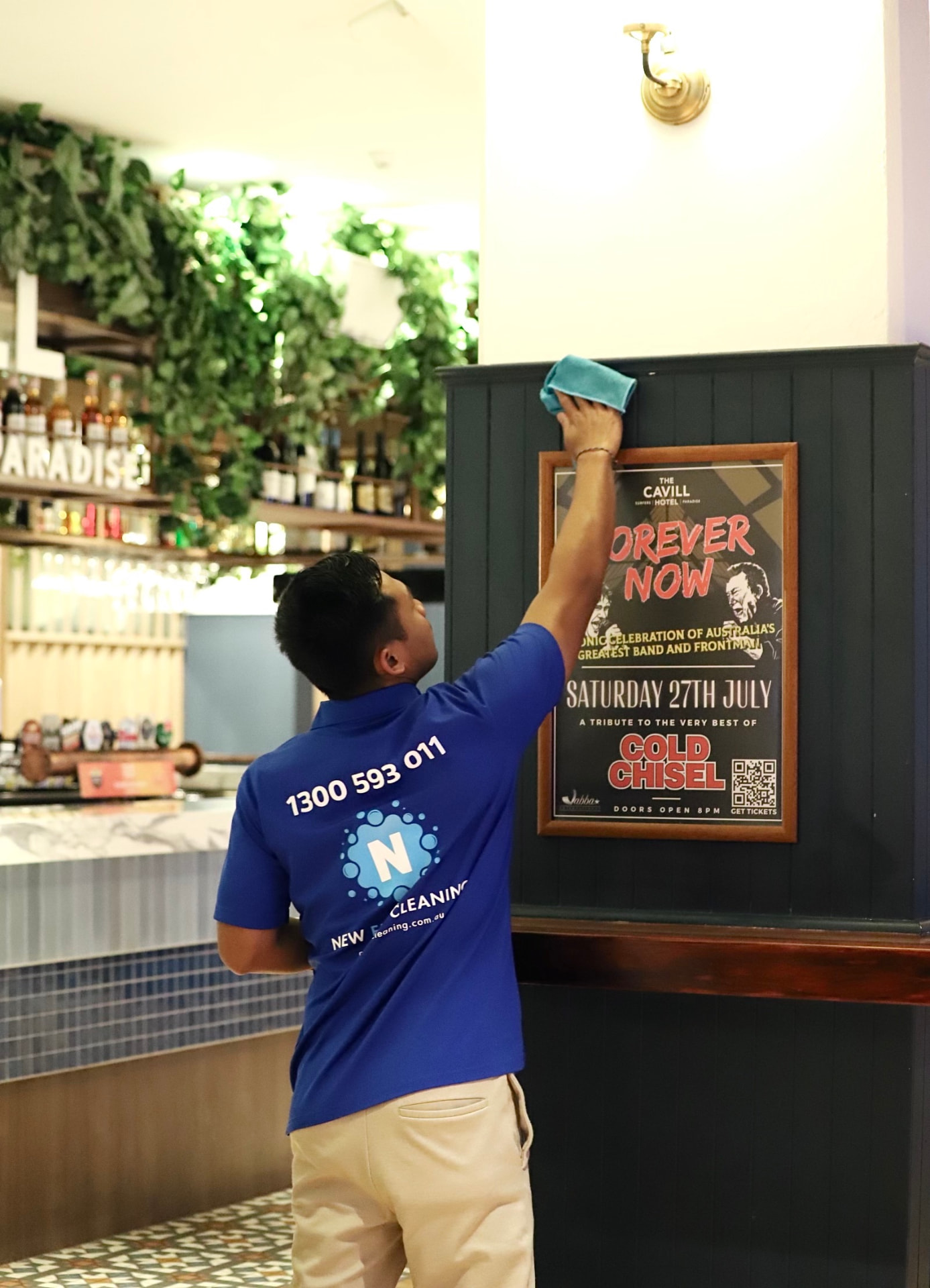 New Era team member in a branded blue polo wiping down a poster surround inside a bar and restaurant venue
