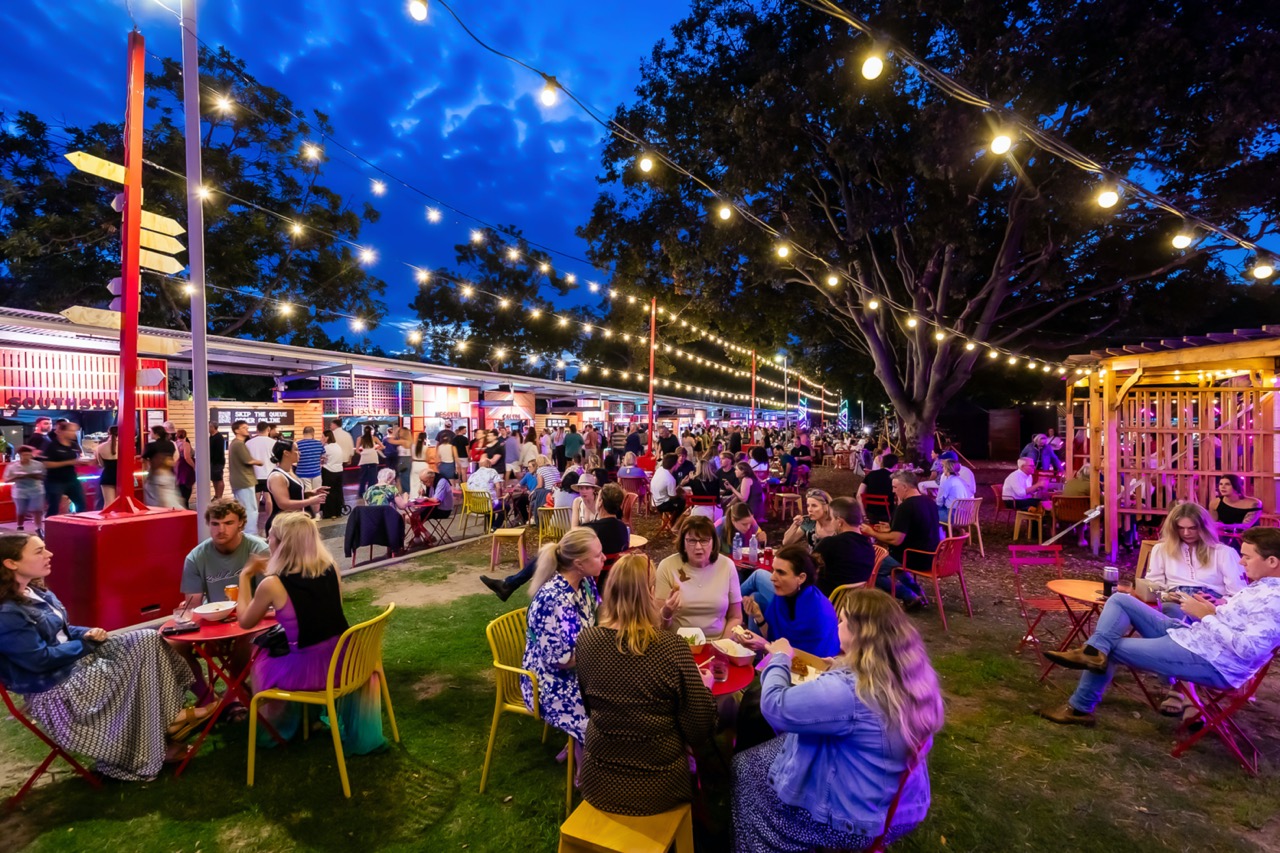 Guests dining under festoon lighting on the lawn at Night Feast