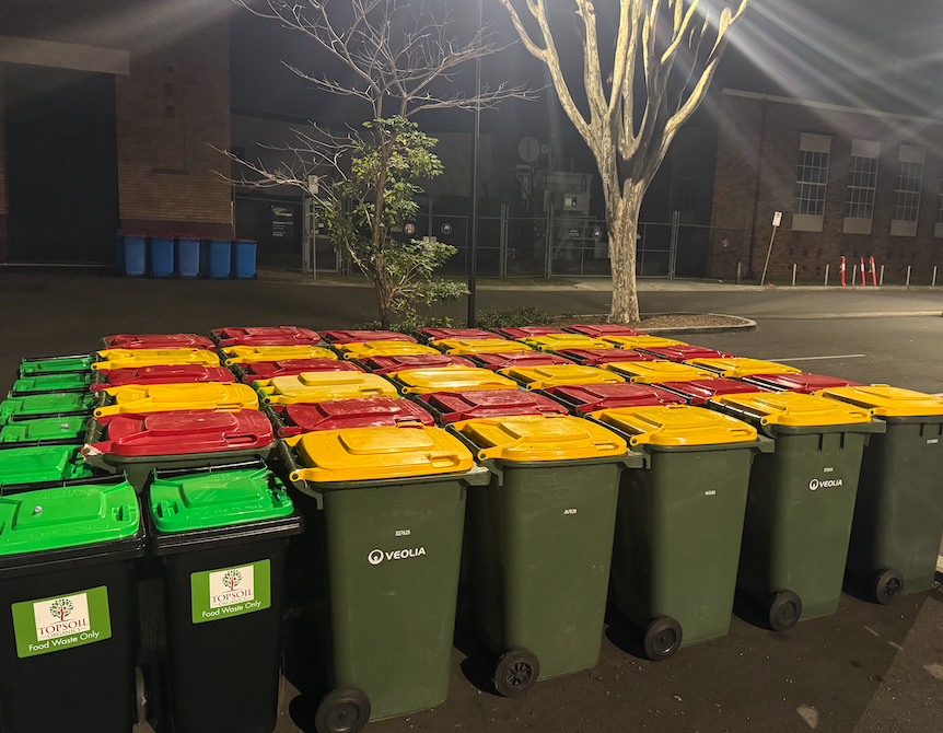 Rows of red-lid, yellow-lid and organics event bins staged in a car park at Night Feast ready for servicing