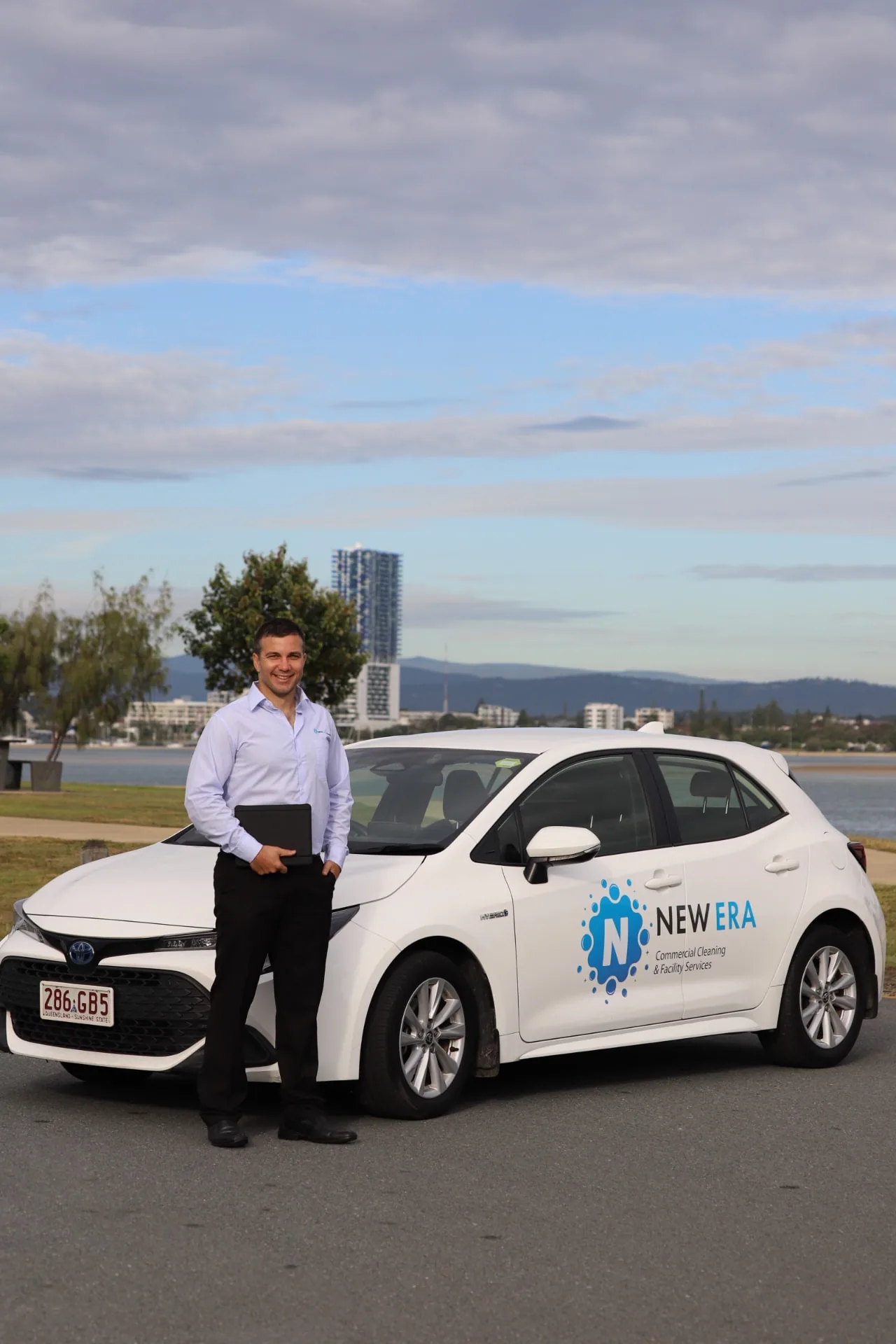 A New Era manager standing with a tablet beside a branded New Era service vehicle on the waterfront