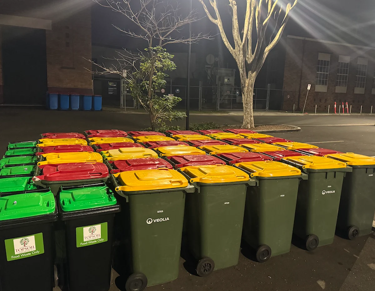Rows of colour-coded event waste bins staged in an external bin compound at night