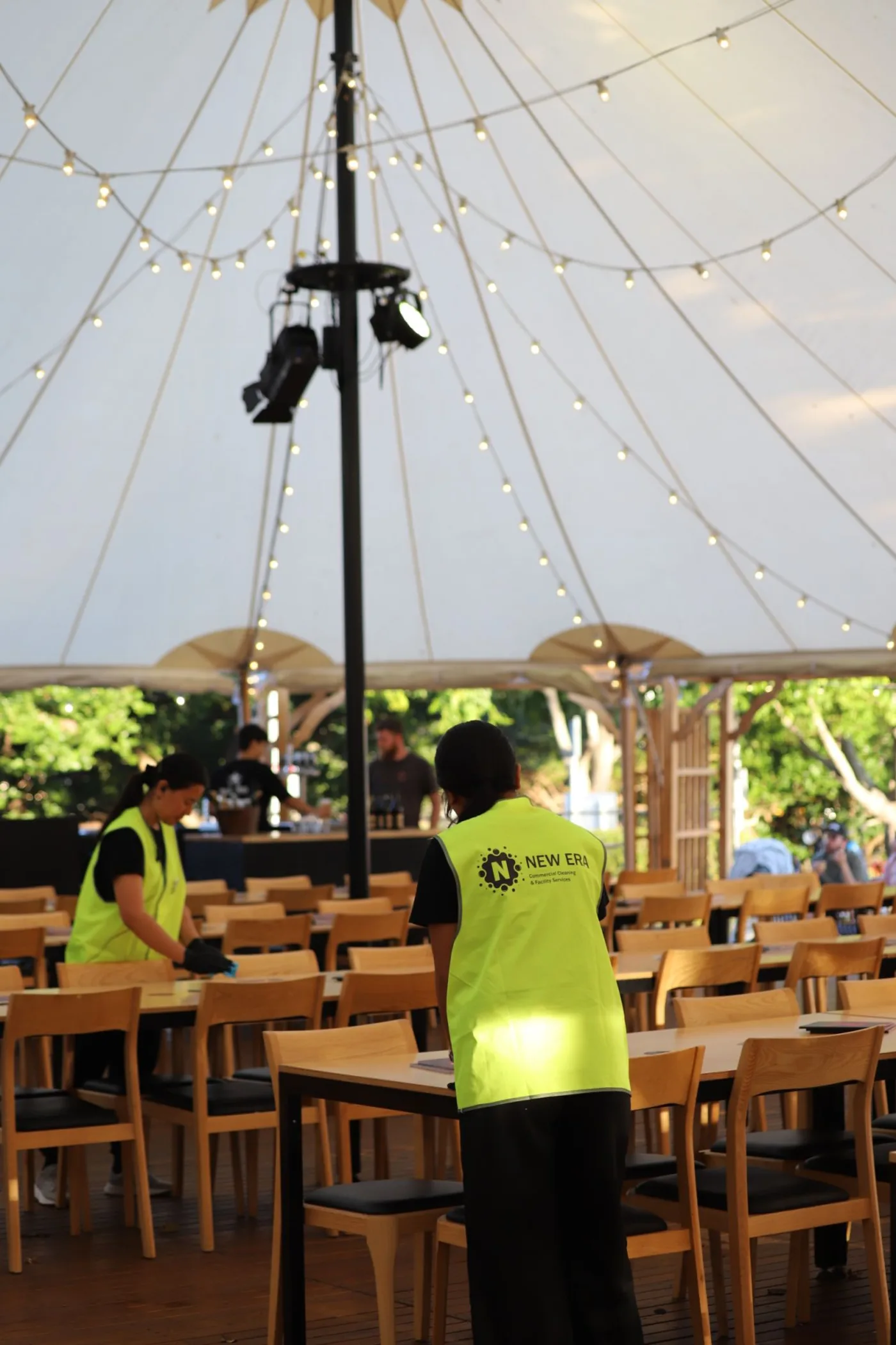 New Era team members resetting and wiping down long dining tables under a festival marquee